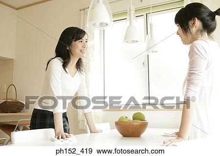 Mid adult woman and her daughter standing beside a table and talking to each other View Large Photo Image Stock Photo - Mid adult woman and her daughter standing beside a table and talking to each other. Fotosearch