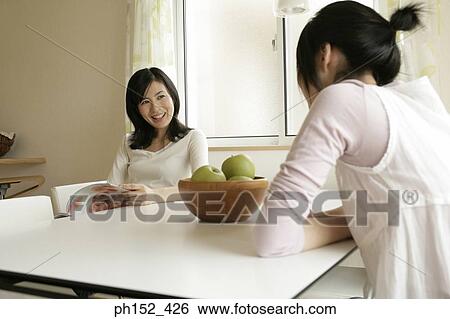 Mid adult woman and her daughter sitting at the table and talking to each other View Large Photo Image Stock Photograph - Mid adult woman and her daughter sitting at the table and talking to each other. Fotosearch