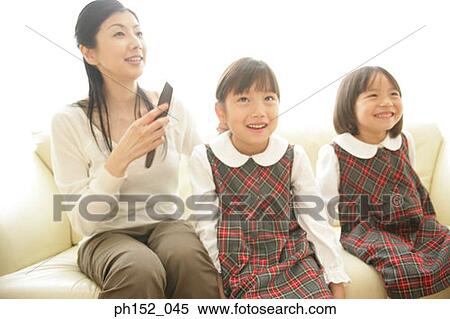 Mid adult woman and her daughters sitting on a couch and smiling View Large Photo Image Stock Photography - Mid adult woman and her daughters sitting on a couch and smiling. Fotosearch