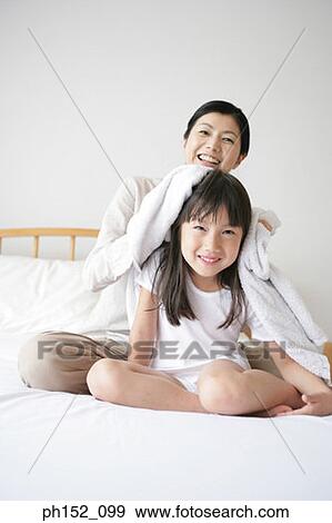 Mid adult woman drying her daughter's hair on the bed and smiling View Large Photo Image Stock Photo - Mid adult woman drying her daughter's hair on the bed and smiling. Fotosearch