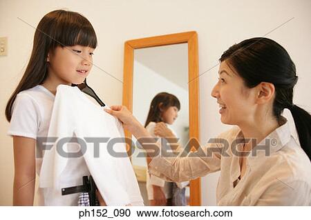 Stock Image - Mid adult woman trying a dress on her daughter. Fotosearch