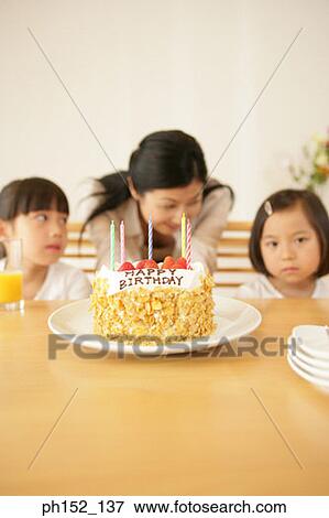 Mid adult woman with her daughters sitting at the table with a birthday cake in front of them View Large Photo Image Stock Photo - Mid adult woman with her daughters sitting at the table with a birthday cake in front of them. Fotosearch
