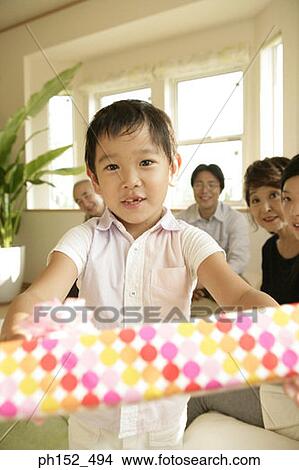 Picture - Portrait of a boy holding a gift with his family in the background. Fotosearch