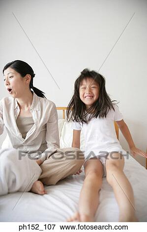 Portrait of a girl jumping on the bed with her mother sitting beside her View Large Photo Image Stock Photo - Portrait of a girl jumping on the bed with her mother sitting beside her. Fotosearch
