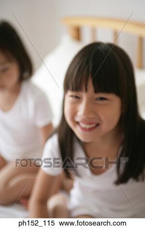 Stock Photography - Portrait of a girl sitting with her sister on the bed and smiling. Fotosearch