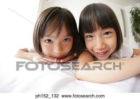 Portrait of a girl with her sister lying on the bed and smiling View Large Photo Image Stock Image - Portrait of a girl with her sister lying on the bed and smiling. Fotosearch