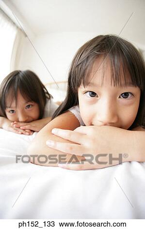 Stock Image - Portrait of a girl with her sister lying on the bed. Fotosearch