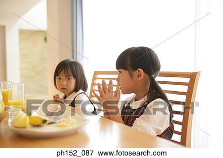 Portrait of a girl with her sister sitting at the dining table and praying View Large Photo Image Stock Photo - Portrait of a girl with her sister sitting at the dining table and praying. Fotosearch
