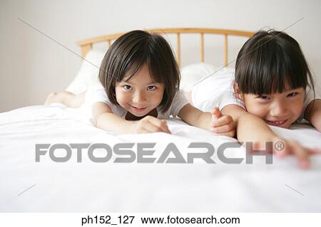 Portrait of a girl with her sister lying on the bed and smiling View Large Photo Image Stock Photo - Portrait of a girl with her sister lying on the bed and smiling. Fotosearch