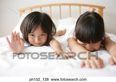 Portrait of a girl with her sister lying on the bed and smiling View Large Photo Image Stock Photo - Portrait of a girl with her sister lying on the bed and smiling. Fotosearch