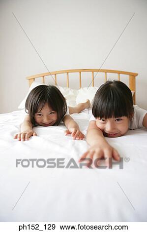 Stock Photo - Portrait of a girl with her sister lying on the bed and smiling. Fotosearch