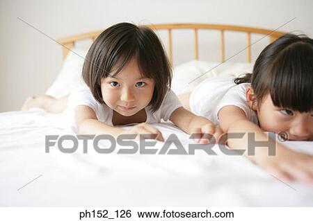 Portrait of a girl with her sister lying on the bed View Large Photo Image Stock Photograph - Portrait of a girl with her sister lying on the bed. Fotosearch