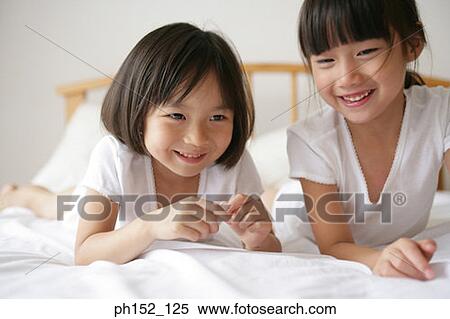Stock Photography - Portrait of a girl with her sister lying on the bed and smiling. Fotosearch