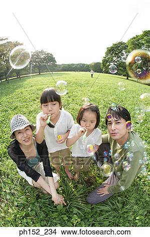Portrait of a mid adult couple and their two daughters blowing bubbles in a park View Large Photo Image Picture - Portrait of a mid adult couple and their two daughters blowing bubbles in a park. Fotosearch