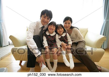 Portrait of a mid adult couple and their daughters sitting on a couch and smiling View Large Photo Image Stock Image - Portrait of a mid adult couple and their daughters sitting on a couch and smiling. Fotosearch