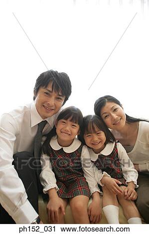 Portrait of a mid adult couple and their daughters sitting on a couch and smiling View Large Photo Image Stock Image - Portrait of a mid adult couple and their daughters sitting on a couch and smiling. Fotosearch