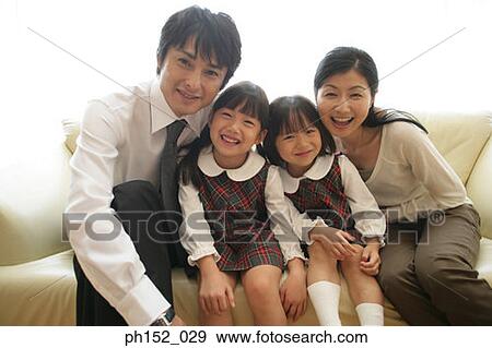 Stock Photo - Portrait of a mid adult couple and their daughters sitting on a couch and smiling. Fotosearch