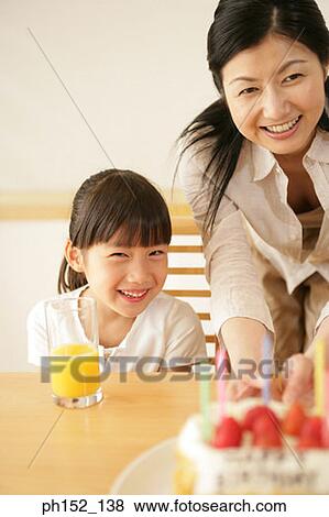 Stock Photo - Portrait of a mid adult woman and her daughter holding a birthday cake on the table. Fotosearch