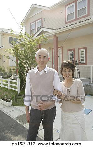 Portrait of a senior couple standing arm in arm in front of a house View Large Photo Image Stock Image - Portrait of a senior couple standing arm in arm in front of a house . Fotosearch