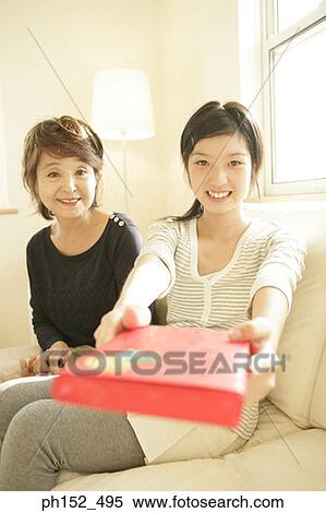 Stock Photography - Portrait of a teenage girl sitting with her grandmother and holding a gift. Fotosearch