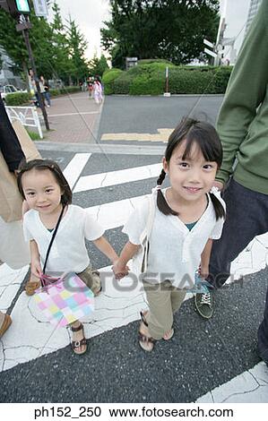 Stock Image - Portrait of two girls crossing the road with their parents. Fotosearch