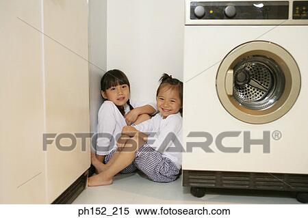 Stock Photography - Portrait of two girls sitting in a corner near a washing machine. Fotosearch