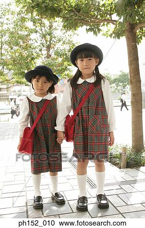 Stock Image - Portrait of two girls standing together and holding hands. Fotosearch