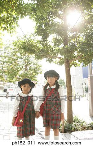 Stock Image - Portrait of two girls standing together and holding hands. Fotosearch
