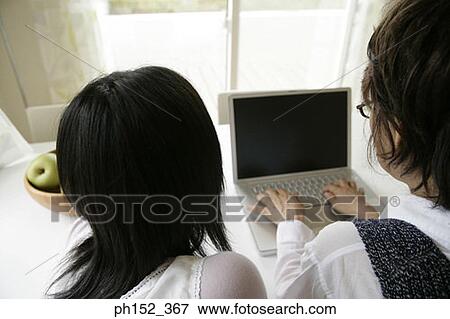 Stock Photo - Rear view of a senior woman using a laptop and her granddaughter sitting beside her. Fotosearch