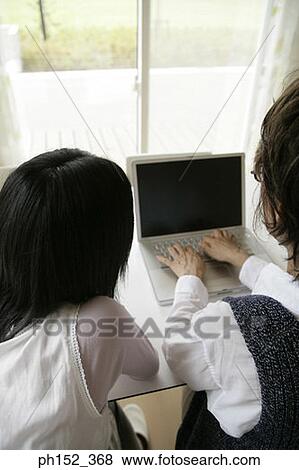 Stock Photo - Rear view of a senior woman using a laptop and her granddaughter sitting beside her. Fotosearch