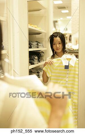 Stock Photography - Reflection of a teenage girl in a mirror holding a t-shirt in a clothing store. Fotosearch