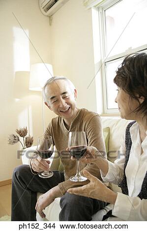 Picture - Senior couple sitting on a couch and holding glasses of red wine. Fotosearch