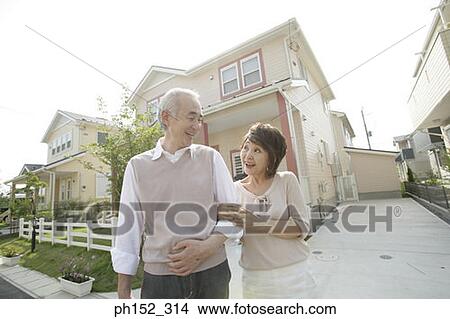 Senior couple standing arm in arm in front of a house and smiling View Large Photo Image Picture - Senior couple standing arm in arm in front of a house and smiling. Fotosearch