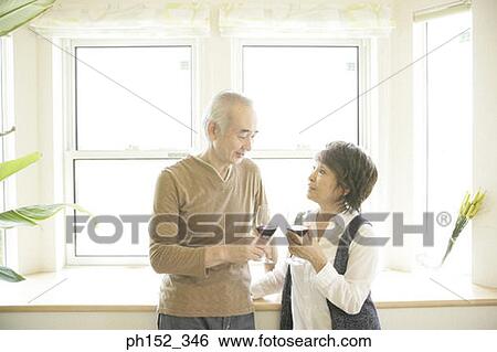 Senior couple standing near a window and holding glasses of red wine View Large Photo Image Stock Photograph - Senior couple standing near a window and holding glasses of red wine. Fotosearch
