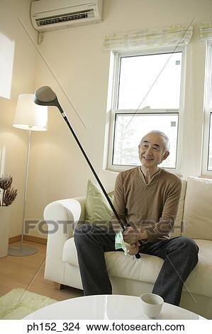 Senior man sitting on a couch and holding a golf club View Large Photo Image Picture - Senior man sitting on a couch and holding a golf club. Fotosearch