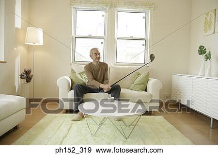 Senior man sitting on a couch and holding a golf club View Large Photo Image Stock Photo - Senior man sitting on a couch and holding a golf club. Fotosearch
