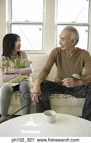 Stock Photo - Senior man sitting on a couch with his granddaughter and smiling. Fotosearch