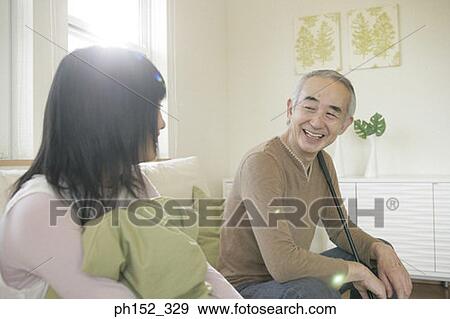 Stock Photo - Senior man sitting on a couch with his granddaughter and smiling. Fotosearch