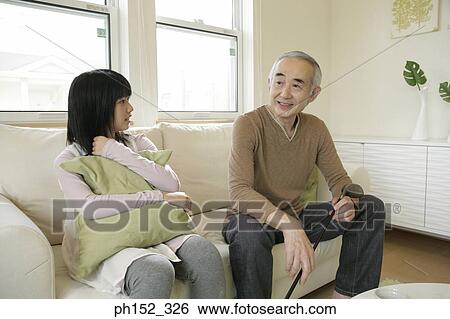 Senior man sitting on a couch with his granddaughter View Large Photo Image Stock Photograph - Senior man sitting on a couch with his granddaughter. Fotosearch