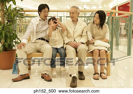 Stock Image - Senior man with his son and grandchildren sitting on a bench in a shopping mall. Fotosearch