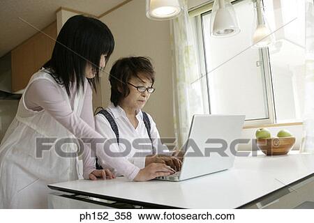 Senior woman using a laptop with her granddaughter standing beside her View Large Photo Image Stock Photo - Senior woman using a laptop with her granddaughter standing beside her. Fotosearch