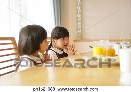 Side profile of a girl and her sister sitting at the dining table and praying View Large Photo Image Stock Photo - Side profile of a girl and her sister sitting at the dining table and praying. Fotosearch