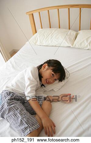 Stock Image - Side profile of a girl lying on the bed and smiling. Fotosearch