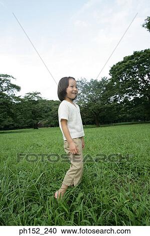 Stock Image - Side profile of a girl standing in the park. Fotosearch
