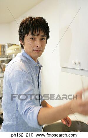 Stock Image - Side profile of a mid adult man washing a glass in the kitchen. Fotosearch