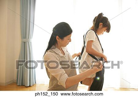 Stock Image - Side profile of a mid adult woman helping her daughter wear a dress. Fotosearch