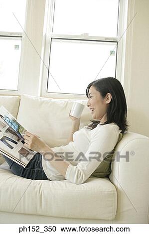 Stock Image - Side profile of a mid adult woman holding a magazine and a coffee cup. Fotosearch