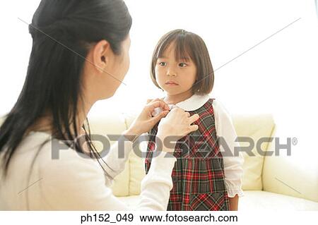Stock Photo - Side profile of a mid adult woman buttoning her daughter's school uniform. Fotosearch