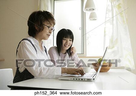Side profile of a senior woman using a laptop with her granddaughter sitting beside her View Large Photo Image Picture - Side profile of a senior woman using a laptop with her granddaughter sitting beside her. Fotosearch