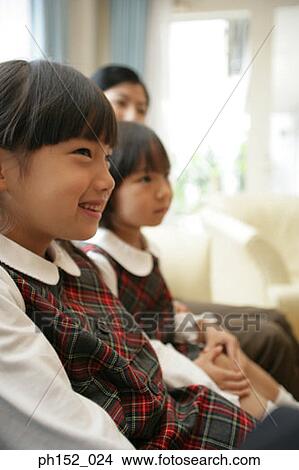 Picture - Side profile of two girls and their mother sitting on a couch. Fotosearch